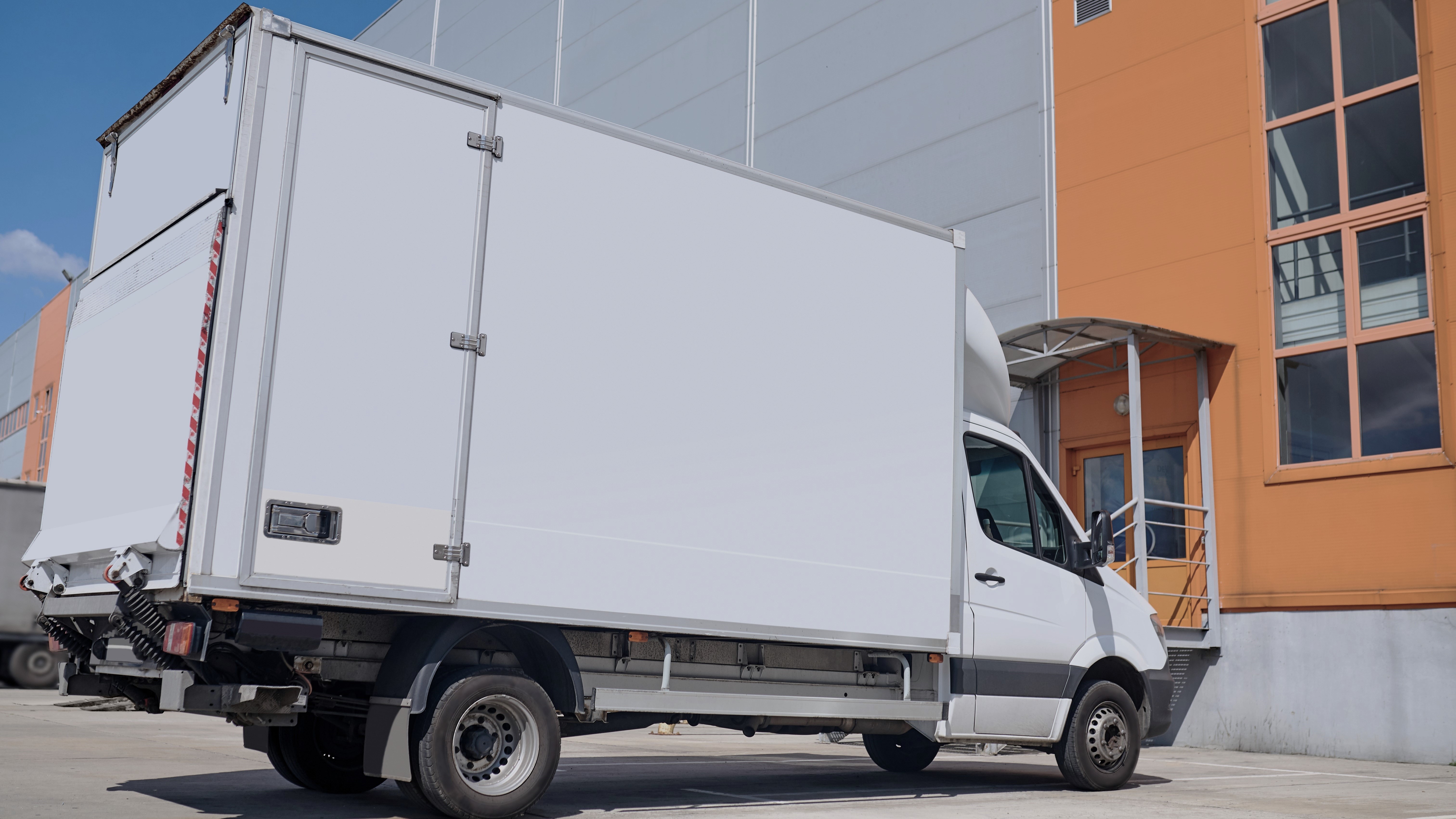 Car, warehouse. White cargo covered vehicle standing outdoors in parking lot near warehouse on fine day